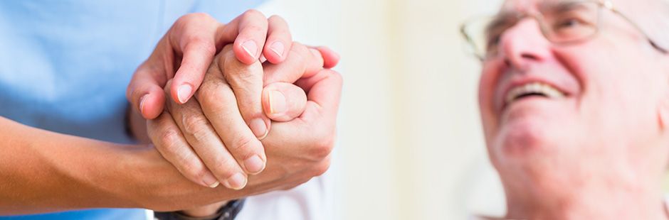 Pflegekraft hält Hand eines männlichen Patienten