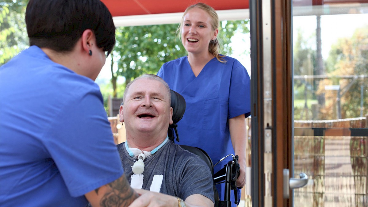 Patient im Rollstuhl mit zwei Pflegekräften, alle lachen