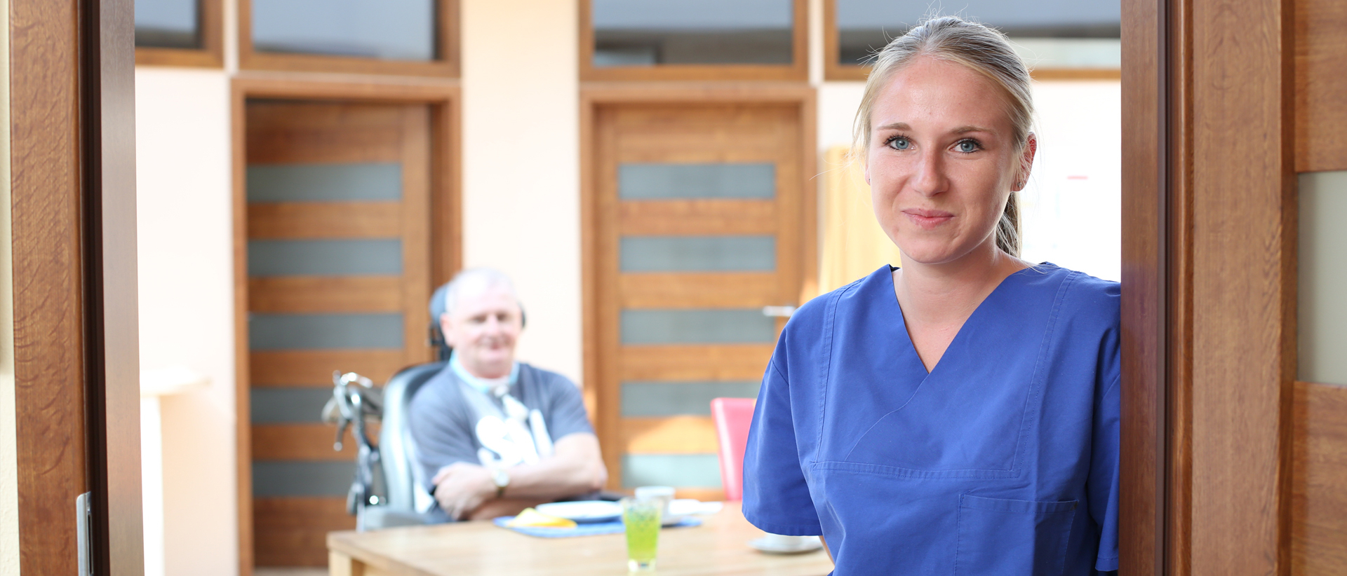 Pflegekraft im blauen Kassack, Patient im Hintergrund