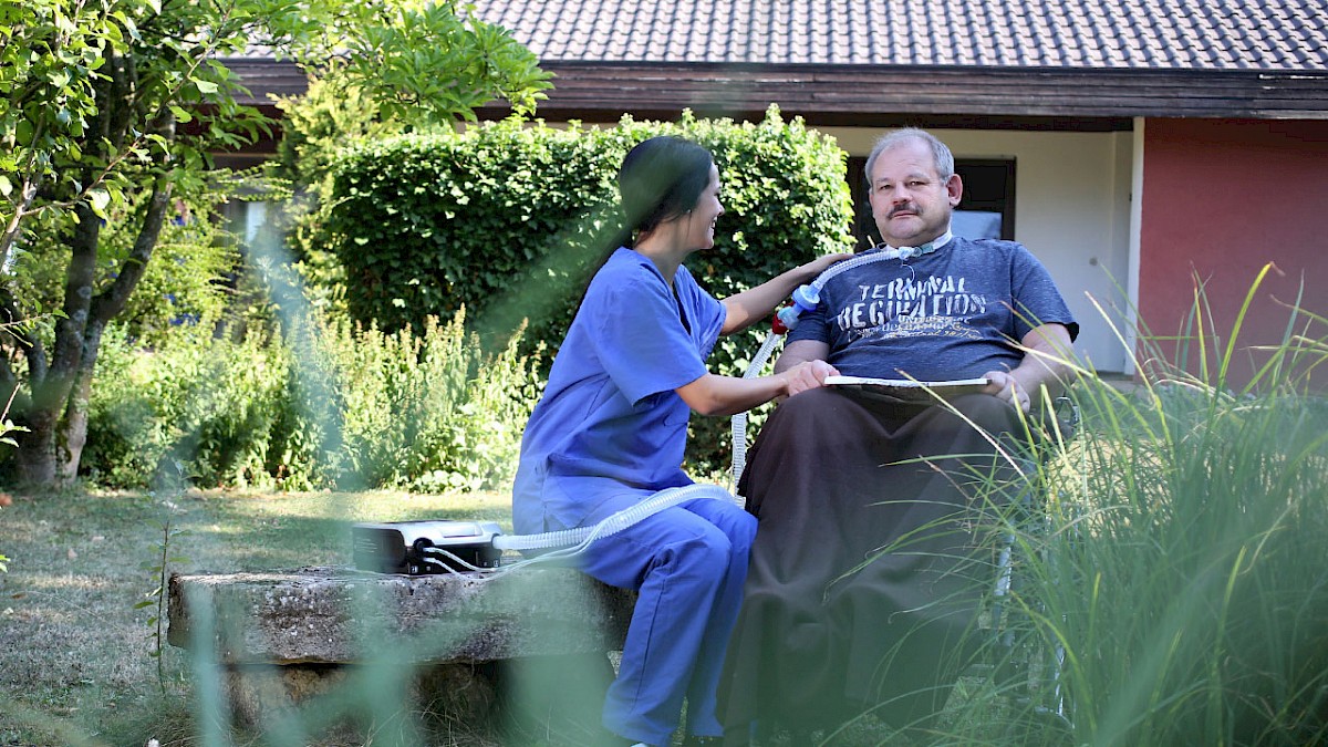 Pflegekraft und Patient im Rollstuhl sitzen im Garten